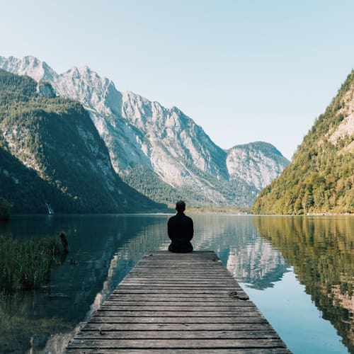 A person sitting on the end of a dock in front of some water