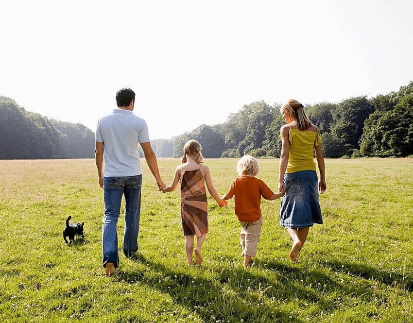 A family walking in the grass with their dog.